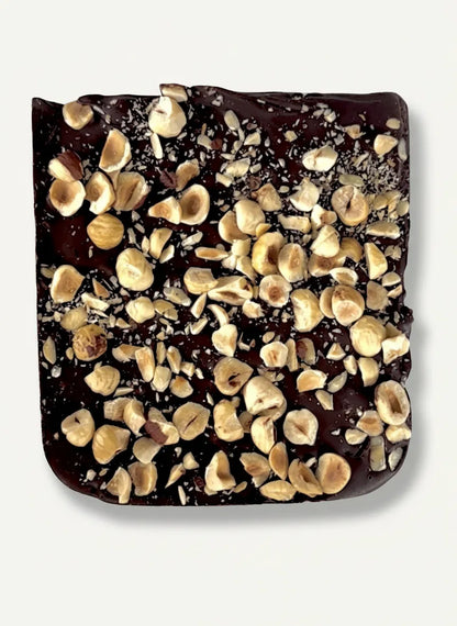 Dark chocolate bar topped with numerous whole and chopped hazelnuts, on a white background.