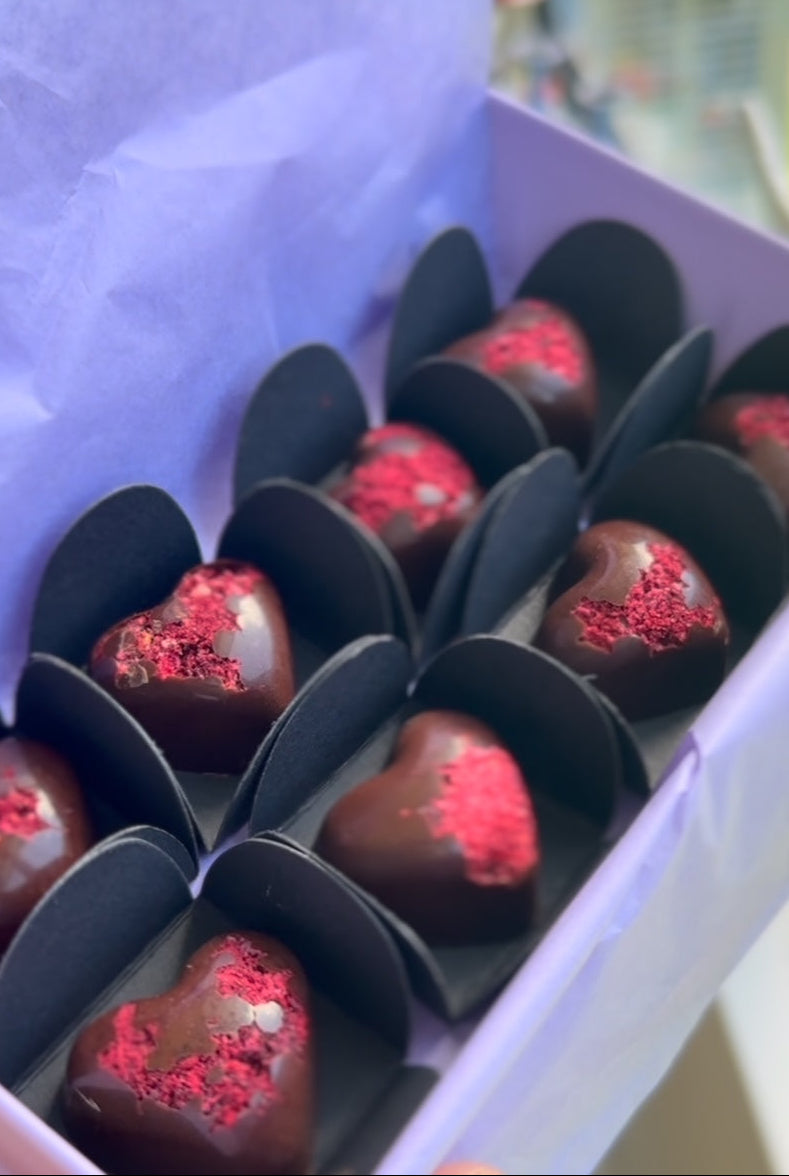Artisan dark chocolate heart-shaped candies with dried raspberry sprinkles in a purple gift box.