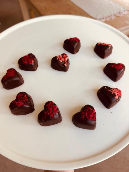 Dark chocolate heart-shaped candies with dried raspberry sprinkles on a white cake stand.