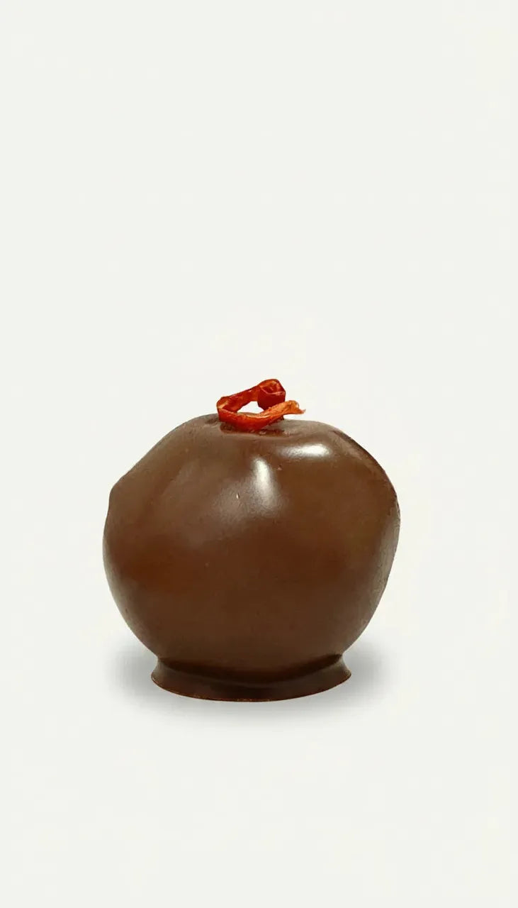 Single dark chocolate truffle with a small red chilli garnish on a white background.