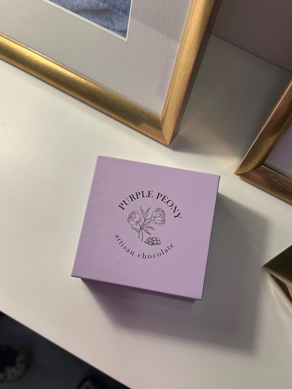 Purple Peony artisan chocolate box, light lavender with black floral logo, on a white surface.