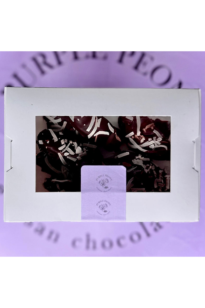 White box of dark chocolate-coated bananas with coconut flakes, on a purple "Purple Peony" background.