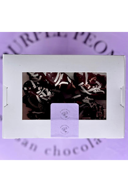 White box of dark chocolate-coated bananas with coconut flakes, on a purple "Purple Peony" background.