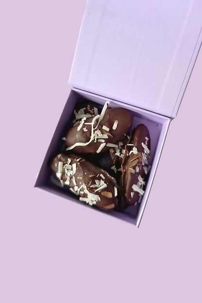 Chocolate-coated bananas with shredded coconut in an open lavender gift box.