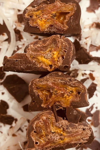 Four dark chocolate-coated banana pieces, cut open to reveal golden fruit, on a bed of coconut flakes.