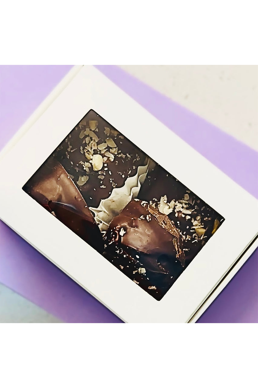 Four dark chocolate-coated prunes with nut sprinkles in a white window box.