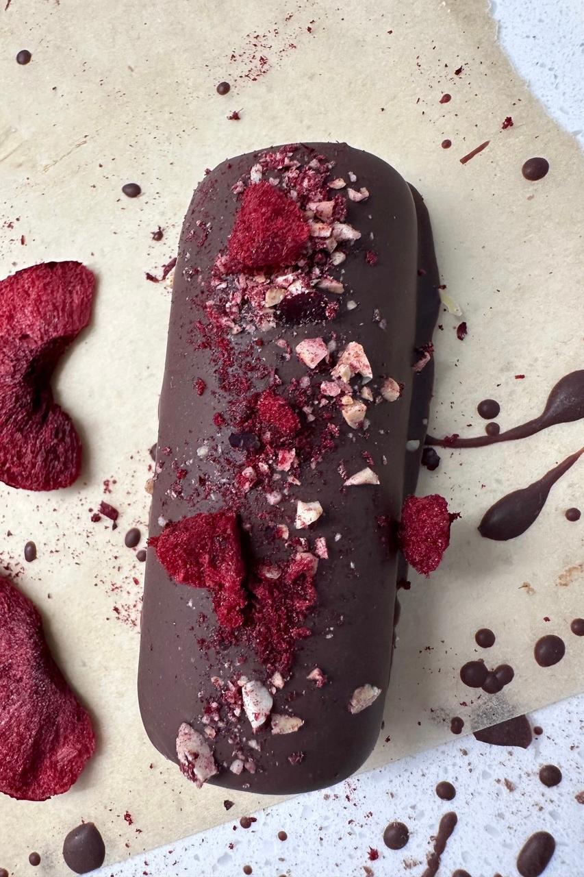 Dark chocolate dessert log topped with vibrant red beetroot powder and chopped nuts on parchment paper.