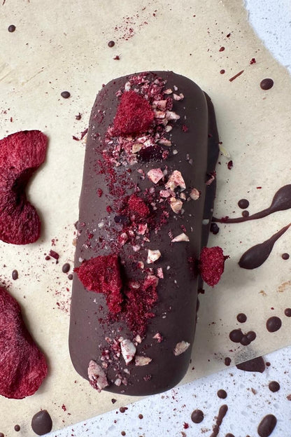 Dark chocolate dessert log topped with vibrant red beetroot powder and chopped nuts on parchment paper.