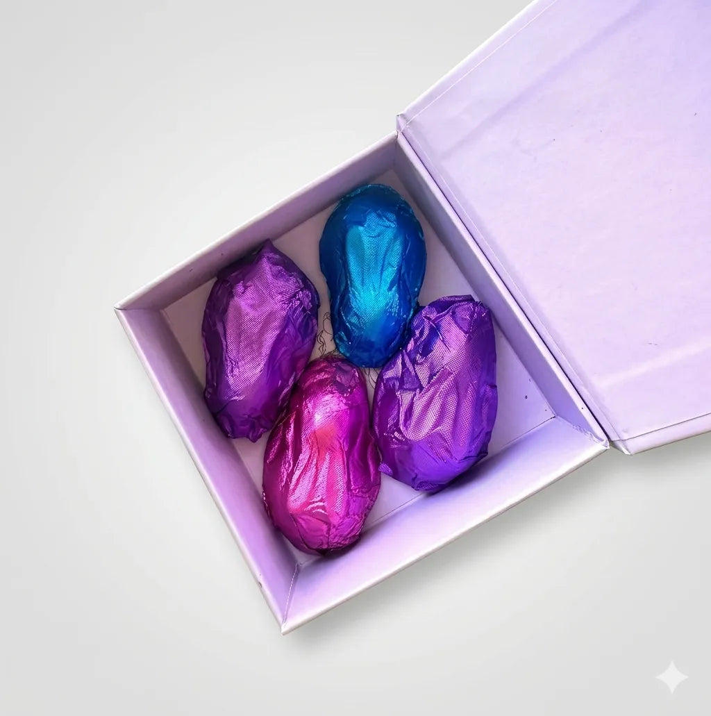 Four foil-wrapped Easter bunny chocolates in a purple box: two dark purple, one bright pink, one blue.