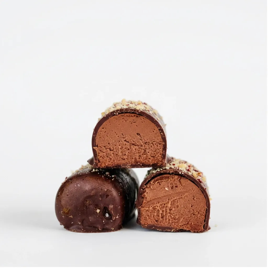 Dark chocolate dessert logs with creamy hazelnut and mango filling, topped with crushed nuts.