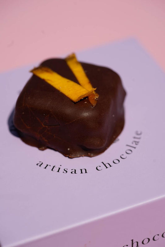 Dark chocolate mango & hazelnut truffle with dried mango strips, on a light purple "artisan chocolate" box.