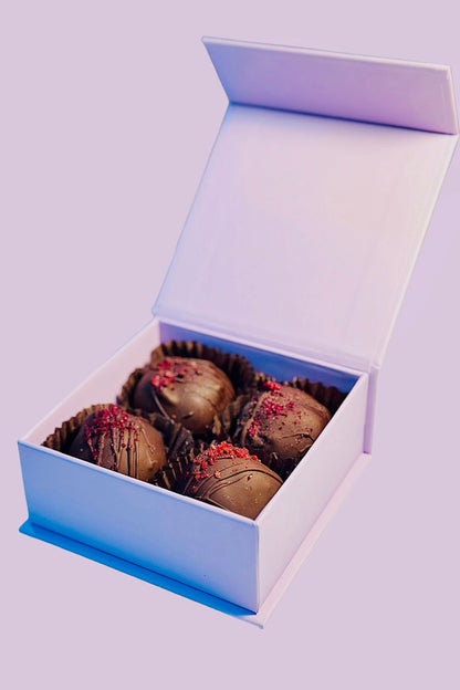 Four dark chocolate Mulled Wine truffles with red sprinkles and drizzle in an open light pink gift box.
