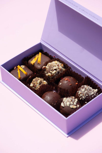 Purple box of 8 handcrafted vegan bonbons: dark chocolate truffles with orange peel, nuts, and red spice.