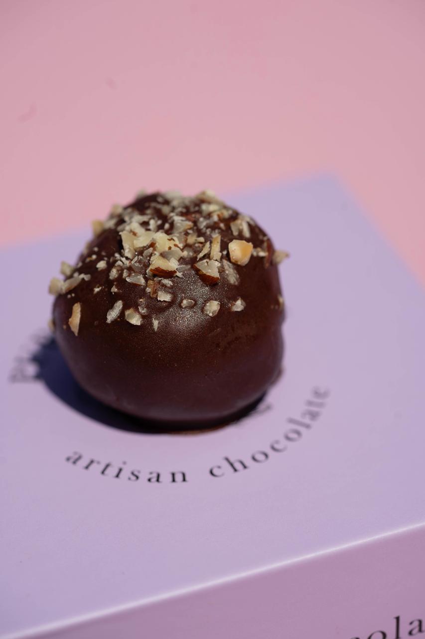 Dark chocolate hazelnut truffle with chopped nuts, on a light purple box.