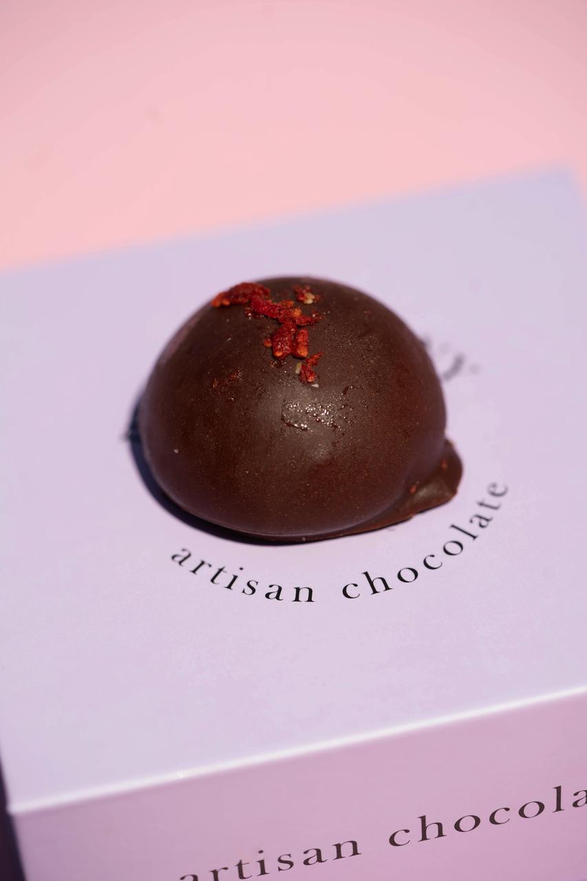 Dark chocolate salted caramel cashew praline with red sprinkles on a light purple "artisan chocolate" box.