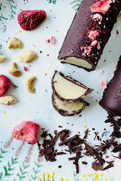 Dark chocolate dessert log, sliced to reveal creamy filling, with cashews, dried strawberries, and chocolate shavings.